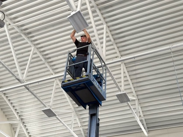 Electrician installing a commercial light fixture from an aerial lift basket