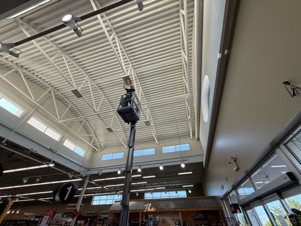 Technician on a boom lift servicing ceiling light fixtures in a retail store