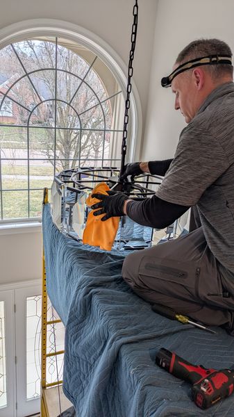 Electrician assembling a metal cage chandelier on a platform beside an arched window