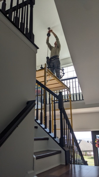 Electrician installing a light fixture above a two-story residential staircase