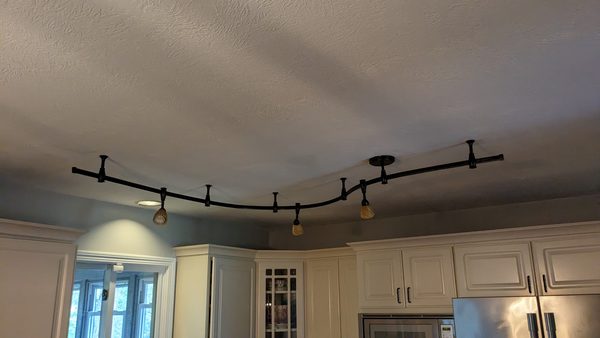 Curved monorail track lighting across a kitchen ceiling