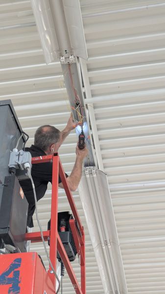 Electrician troubleshooting an overhead junction box from a lift in a metal building