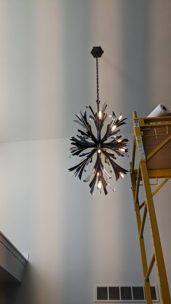 Starburst chandelier hung in a two-story room, with the ladder still set from the install