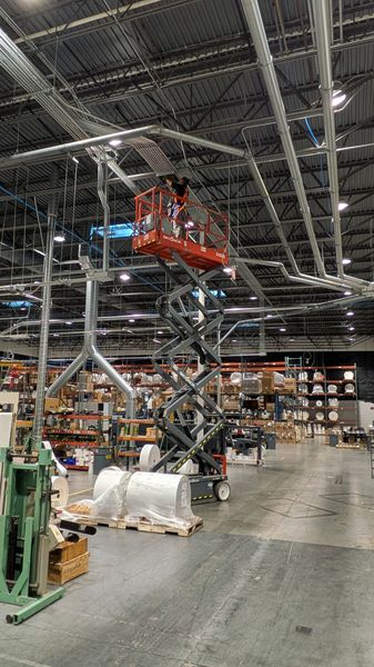 Scissor lift raised for overhead conduit work in a warehouse