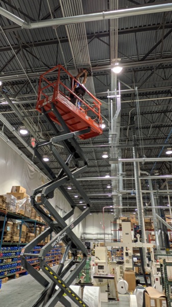 Scissor lift raised for high-bay lighting and conduit work in a warehouse