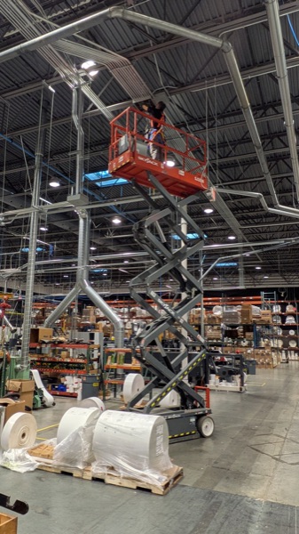 Conduit and high-bay lighting installation from a scissor lift in a warehouse