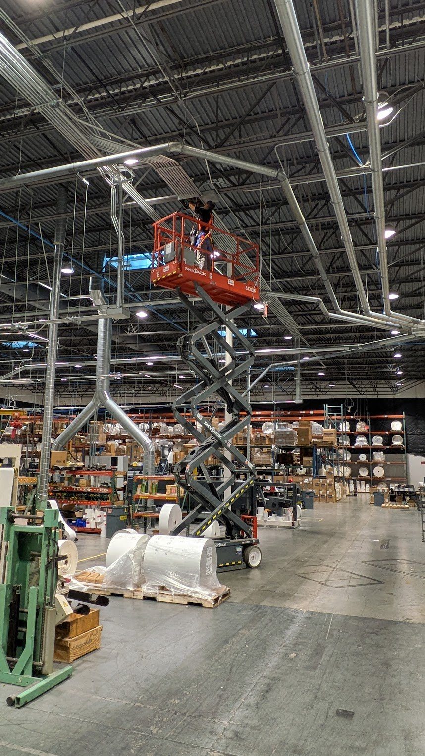 Overhead conduit and lighting runs installed from a scissor lift in a warehouse by Benrishi Electrical