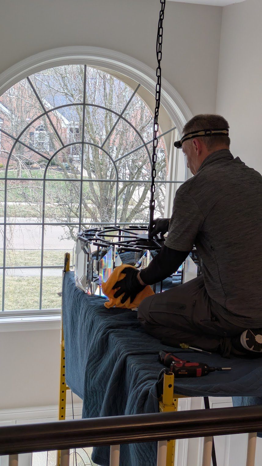 Benrishi Electrical servicing a crystal chandelier on scaffolding by a tall arched window
